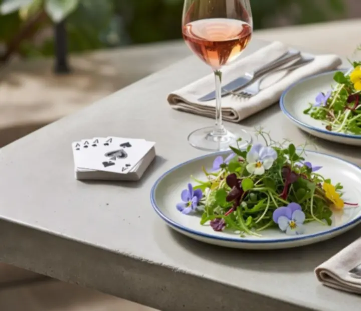 Grande table en béton dressée avec plats contemporains, micro-pousses et jetons de poker.